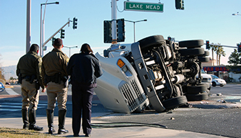 three people looking to an overturned truck in a street intersection, representing truck accidents