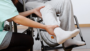 a nurse holding the leg of a patient sitting on a wheelchair, representing serious injury