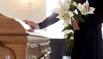 a man in black holding white flowers while touching a coffin, representing wrongful death